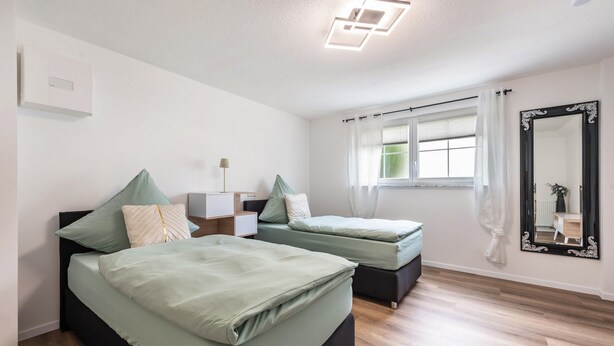 Un dormitorio con dos camas, una mesita de noche, una lámpara, una ventana con cortinas y un espejo.