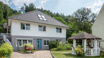 A two-story house with a tiled roof, a front porch, and a small gazebo.