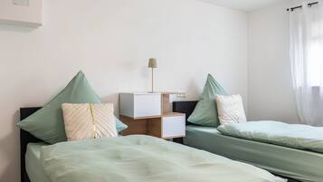 Ein Hotelzimmer mit zwei Betten, einem Nachttisch, einer Lampe und einem Fenster mit Vorhängen.