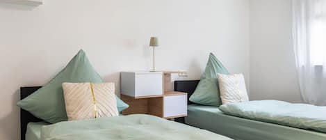 A hotel room with two beds, a bedside table, a lamp, and a window with curtains.