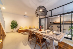 A modern dining area with a long table, wooden chairs, and a hanging light fixture. - Bougenvia Villa (Badung)