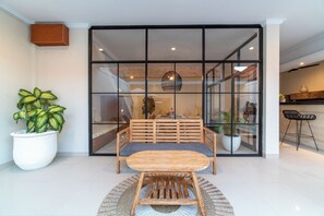 Un interior modern amb una zona de menjador que presenta una taula i cadires de fusta, una planta gran en test i una partició de vidre.