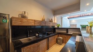 Una cocina moderna con refrigerador de acero inoxidable, armarios de madera, encimera negra y vistas al exterior.