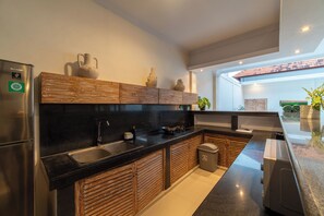 Una cuina moderna amb nevera d'acer inoxidable, armaris de fusta, taulell negre i vista a l'exterior.