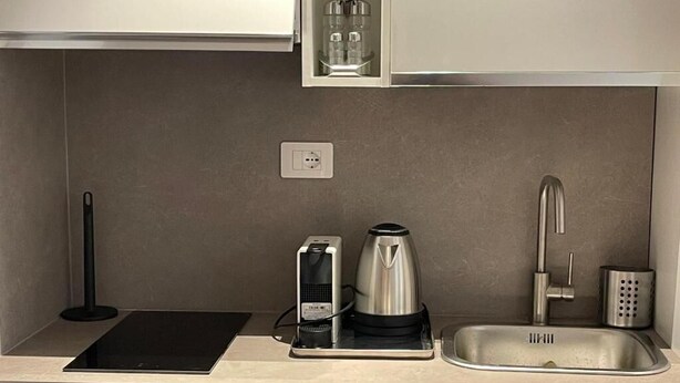 A modern kitchen with a built-in induction cooktop, a kettle, and a stainless steel sink. - Foro Romano Apartments E (Rome)
