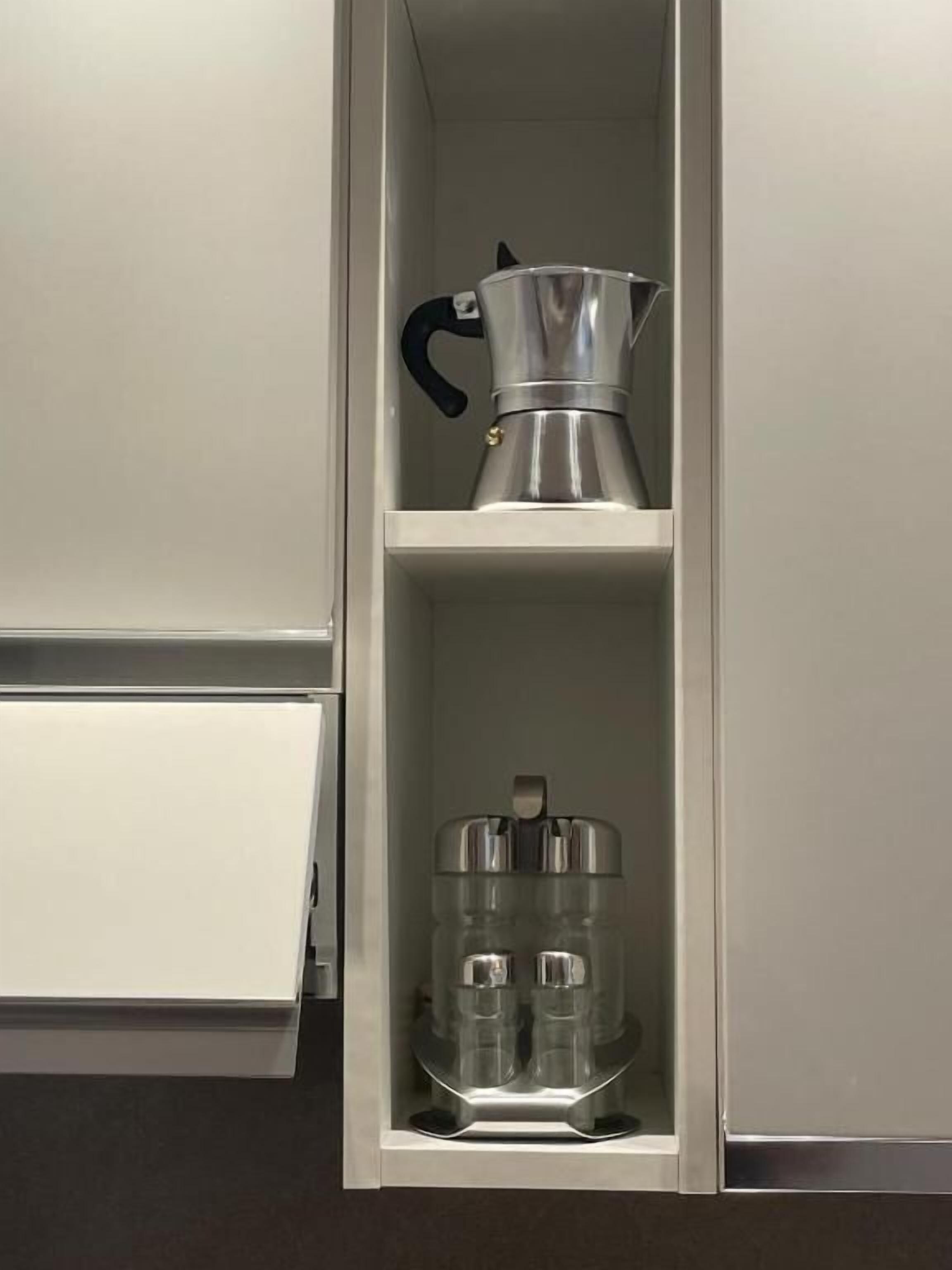 A kitchen cabinet with a coffee maker and two glass containers on the shelf.