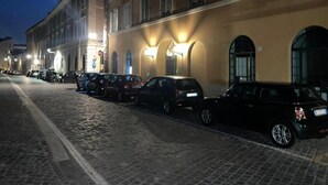 A cobblestone street lined with parked cars and buildings with illuminated signage. - Foro Romano Apartments E (Rome)