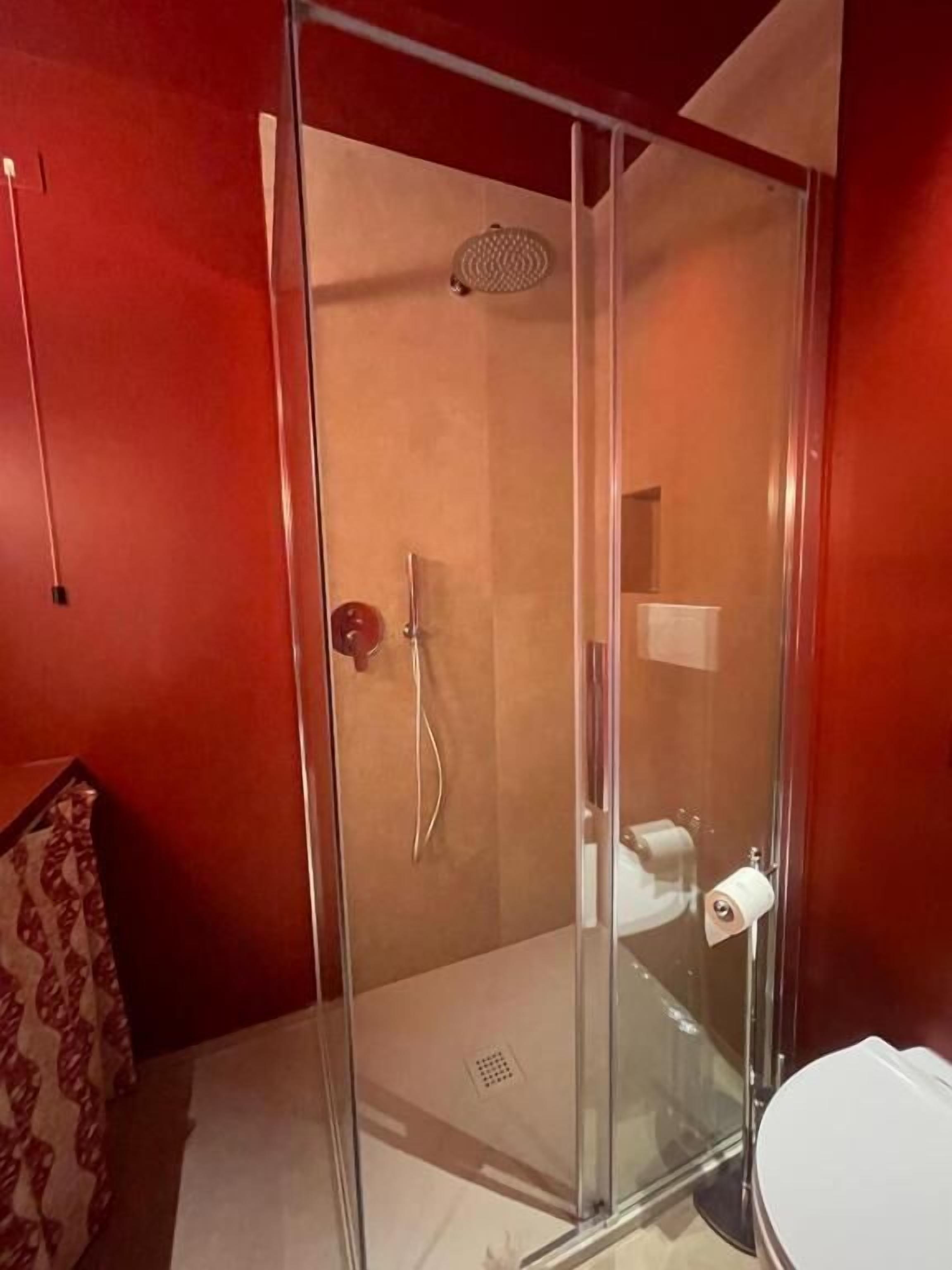 Un vestidor de ducha con paredes de vidrio, cabezal de ducha de mano, inodoro y perchero para toallas.