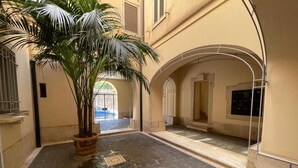 A hotel corridor with stone flooring, a palm tree, and arched doorways. - Foro Romano Apartments E (Rome)