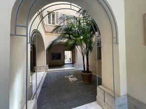 An indoor corridor with a potted palm tree, stone flooring, and arched ceilings. - Foro Romano Apartments E (Rome)