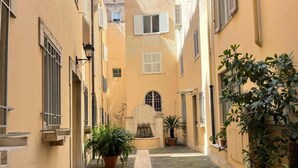 A narrow alleyway with buildings on either side, potted plants, and a stone pathway. - Foro Romano Apartments E (Rome)