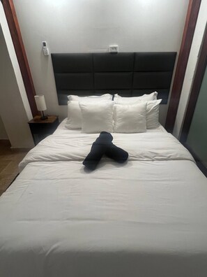 Ein Hotelzimmer mit Bett, Kissen, einem Nachttisch mit Lampe und einer wandmontierten Bedieneinheit.