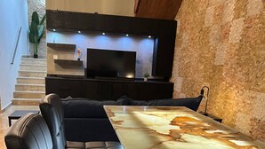 Een moderne eetruimte met een lange tafel, zwarte lederen zitplaatsen en een televisie erboven.