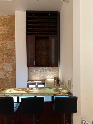 A kitchen with a stone backsplash, wooden cabinets, a bar area with stools, and a built-in wine rack.