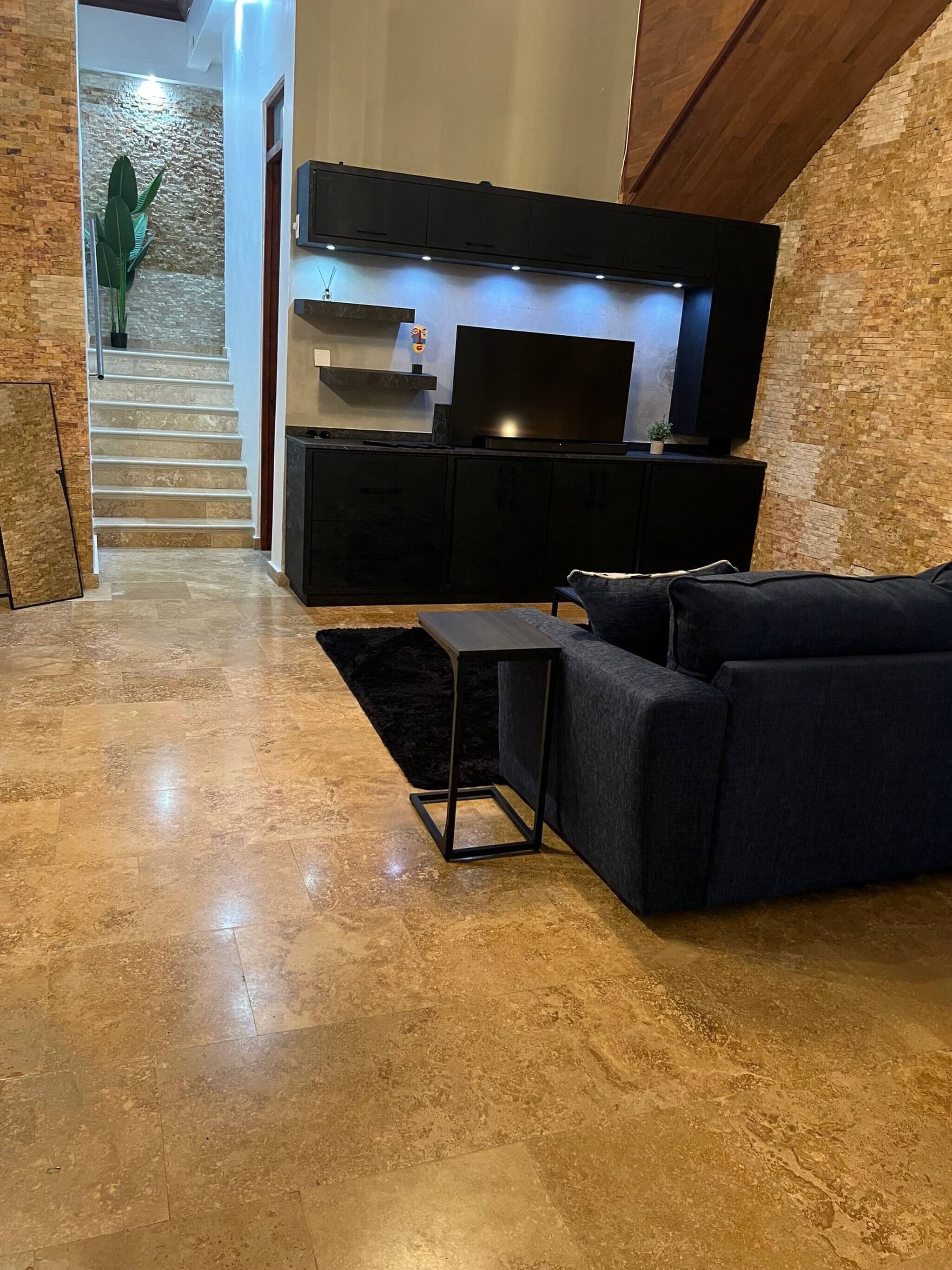 A modern living room with a dark sofa, a small table, and a flat-screen TV mounted on a wall.
