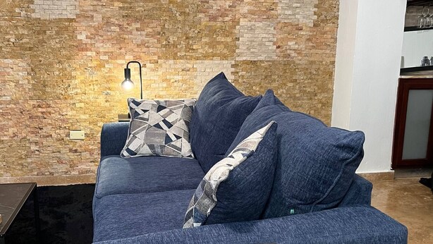 Een moderne woonkamer met een blauwe bank, gekleurde kussens, een bijzettafeltje en een bakstenen muur.