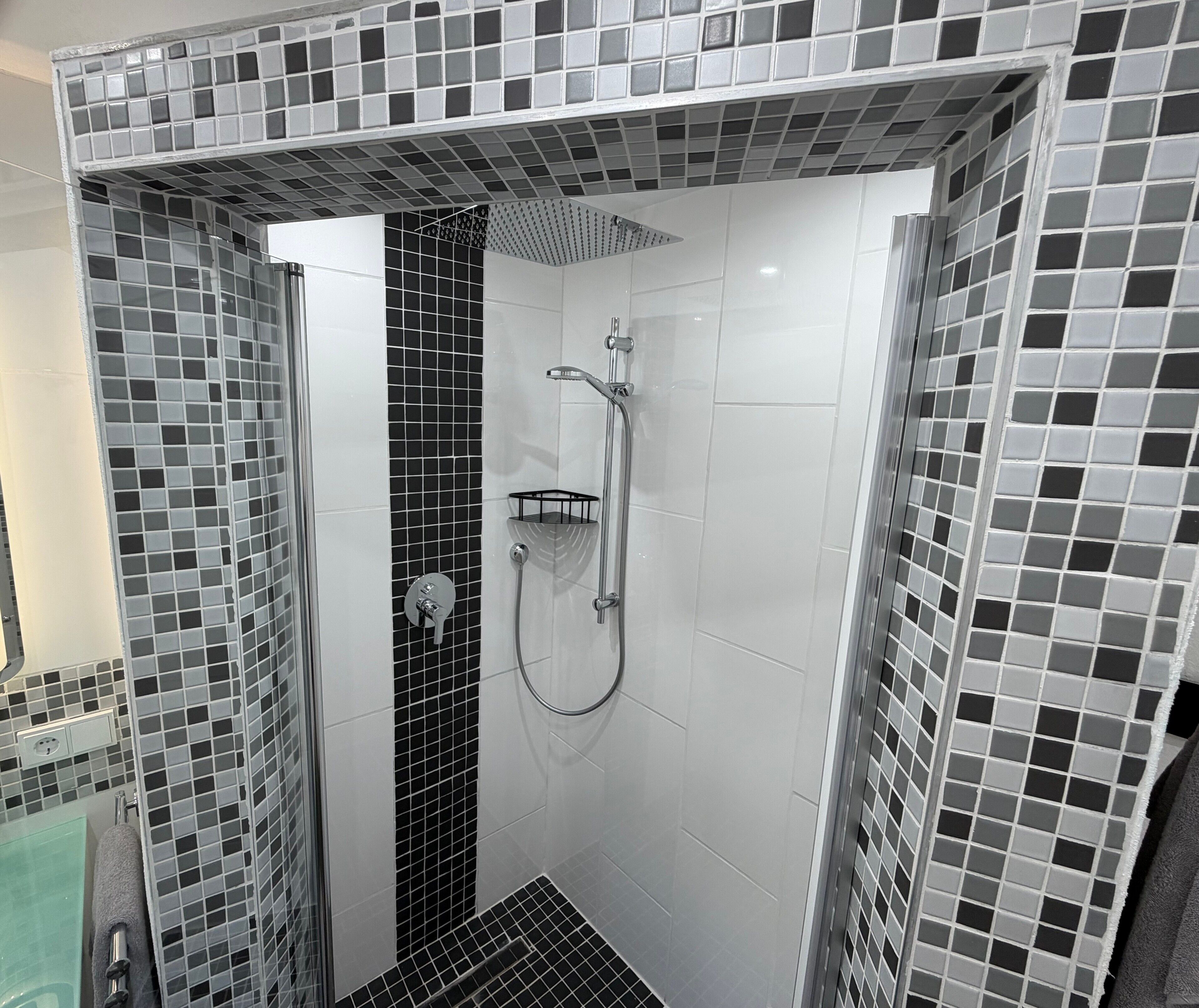 Eine begehbare Dusche mit einer gefliesten Wand, einer Duschköpfe und einem Handbrauseinsatz.