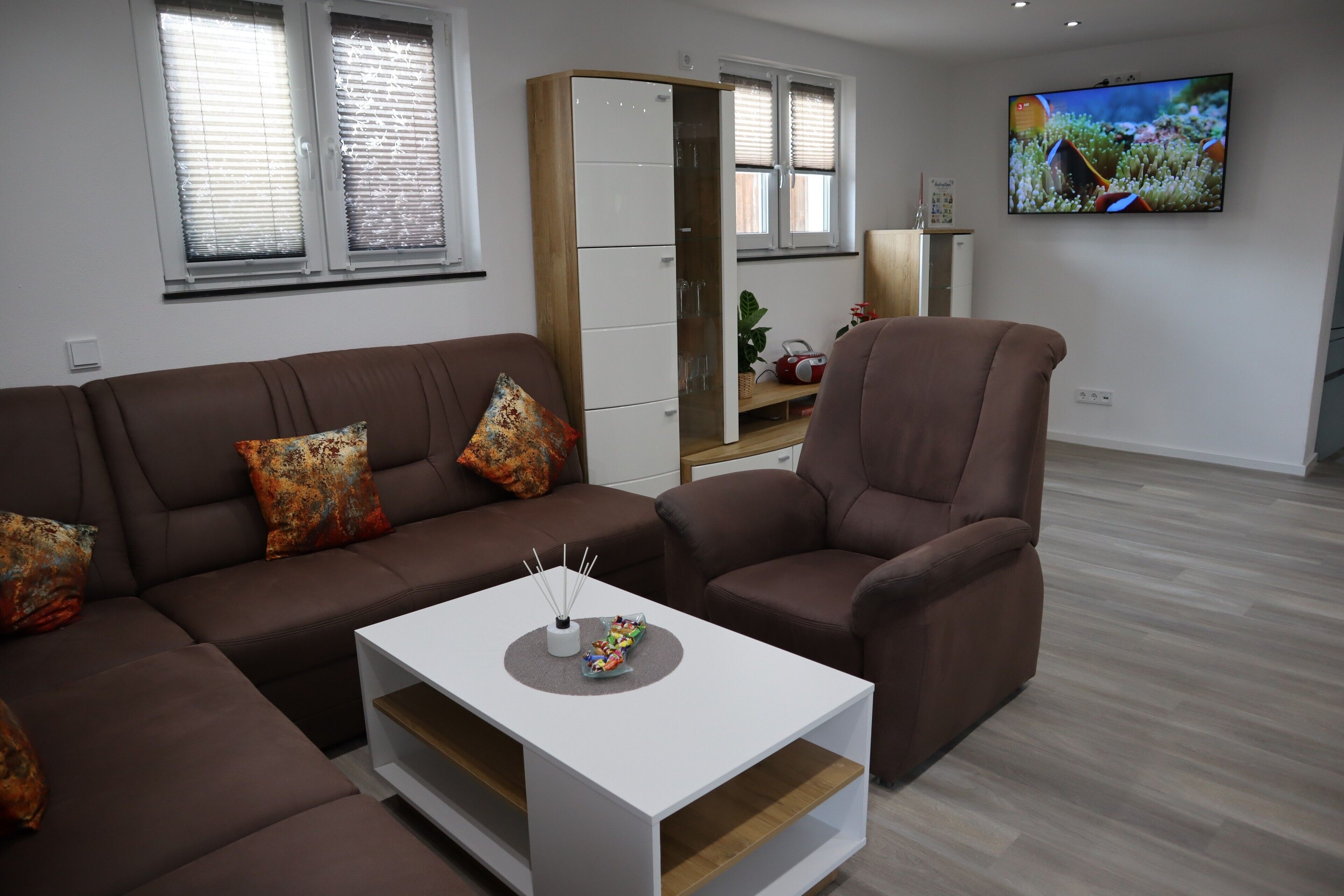 Ett modernt vardagsrum med en brun soffa, ett vitt soffbord och en tv som är monterad på väggen.