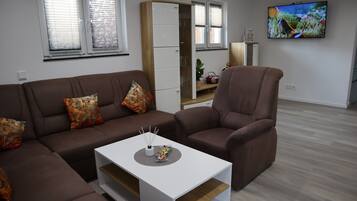 Ett modernt vardagsrum med en brun soffa, ett vitt soffbord och en tv som är monterad på väggen.