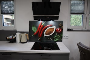 A kitchen with a modern stove, a flat-screen TV, and a window with blinds.