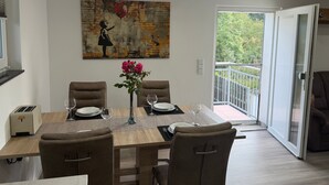 A dining area with a table set for four, chairs, a vase with flowers, and a painting on the wall. - Modern Apartment “Frankenruhe” near Bamberg on the Edge of Franconian Switzerland (Strullendorf)
