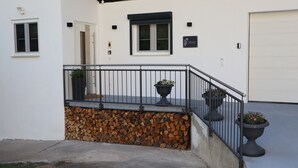 A building with a white exterior, a black metal railing, and a stack of firewood. - Modern Apartment “Frankenruhe” near Bamberg on the Edge of Franconian Switzerland (Strullendorf)