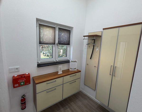 A room with a window, a wooden counter, a cabinet, a wardrobe, and a fire extinguisher.
