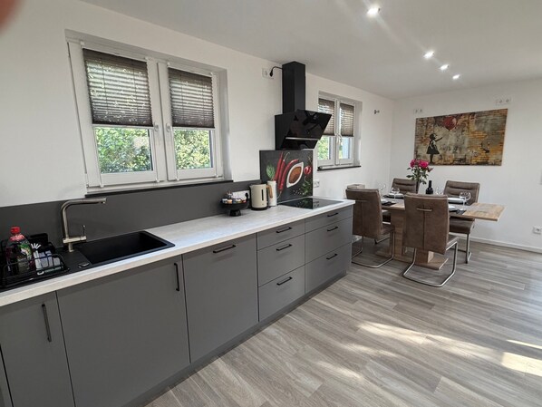 A modern kitchen with a central island, a dining area with a table and chairs, and a painting on the wall.