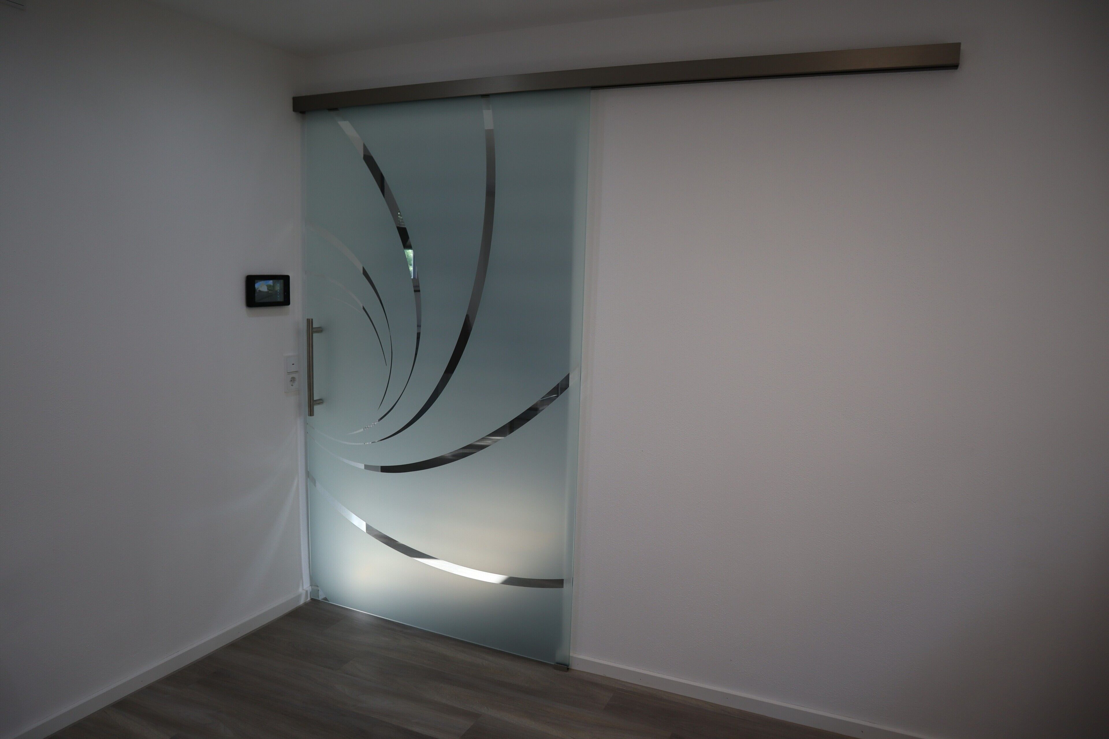 Ein modernes Interieur mit einer Schiebeglastür, die einen dekorativen Metallrahmen und ein kleines, an der Wand befestigtes Gerät aufweist.