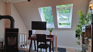 Une pièce avec une cheminée, un bureau avec un ordinateur, deux fenêtres et un ventilateur de plafond.