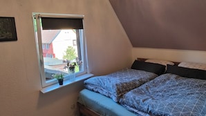 Une chambre avec un plafond en pente, une fenêtre donnant sur des immeubles, un lit avec une literie à motifs et un lustre.