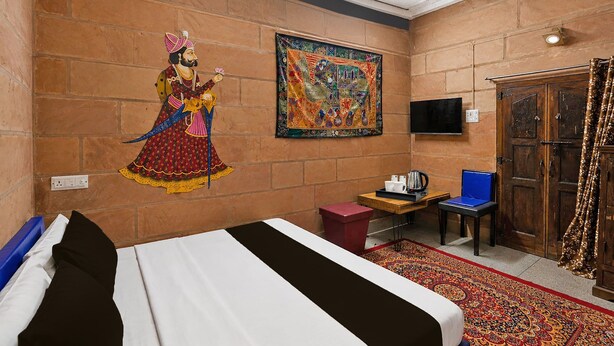 A hotel room with a bed, a small table with a kettle, a chair, a television, and a large mural on the wall. - Collection O Blue City Jodhpur Formerly (Jodhpur)