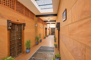 Um corredor com claraboia, plantas em vasos e uma grade de metal.