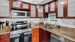 A kitchen with a stainless steel stove, microwave, and oven, wooden cabinets, granite countertop, and a sink. - 1 Block To Beach • Walk To Shops + Dining | Pet Friendly | Poinciana (Lauderdale-by-the-Sea)