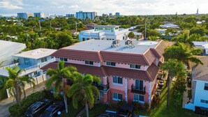 A multi-story residential building with a red-tiled roof, surrounded by palm trees and parked cars. - 1 Block To Beach • Walk To Shops + Dining | Pet Friendly | Poinciana (Lauderdale-by-the-Sea)