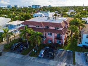 A multi-story residential building with a red-tiled roof, surrounded by palm trees and parked cars. - 1 Block To Beach • Walk To Shops + Dining | Pet Friendly | Poinciana (Lauderdale-by-the-Sea)