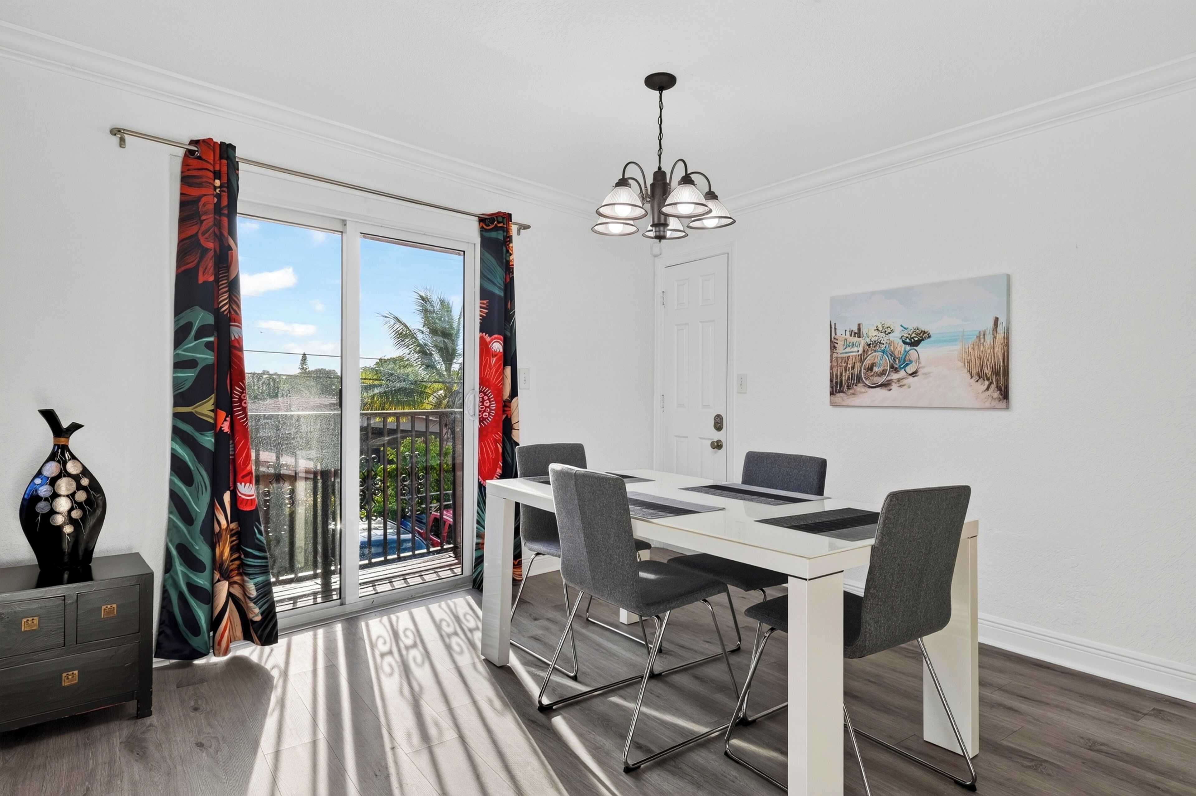 A dining area with a table and chairs, a chandelier, a door, and a painting on the wall.