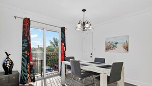 A dining area with a table and chairs, a chandelier, a door, and a painting on the wall. - 1 Block To Beach • Walk To Shops + Dining | Pet Friendly | Poinciana (Lauderdale-by-the-Sea)