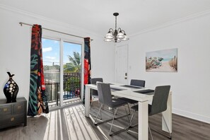 A dining area with a table and chairs, a chandelier, a door, and a painting on the wall. - 1 Block To Beach • Walk To Shops + Dining | Pet Friendly | Poinciana (Lauderdale-by-the-Sea)