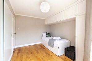 A bedroom with a bed, a chest of drawers, a hanging light fixture, and a wooden floor. - Stylish Hyde Park & Paddington Stay (London)