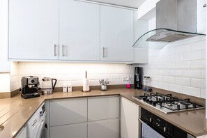A modern kitchen with white cabinets, a gas stove, a coffee maker, and a dishwasher. - Stylish Hyde Park & Paddington Stay (London)
