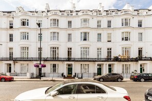 A row of white townhouses with bay windows, a black metal fence, and hanging flower baskets. - Stylish Hyde Park & Paddington Stay (London)