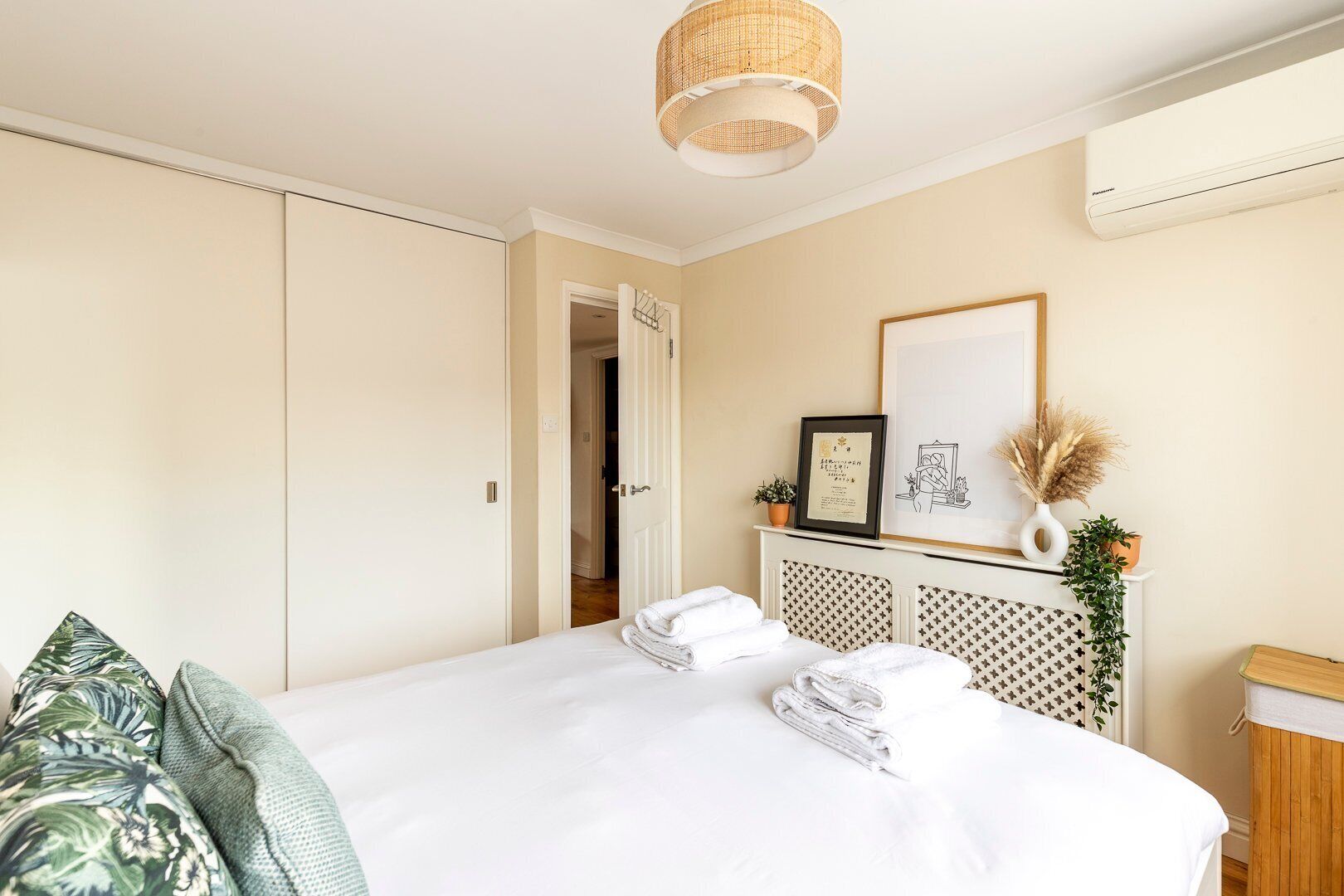 A hotel room with a bed, a wardrobe, a door, a wall-mounted air conditioner, and a framed picture.