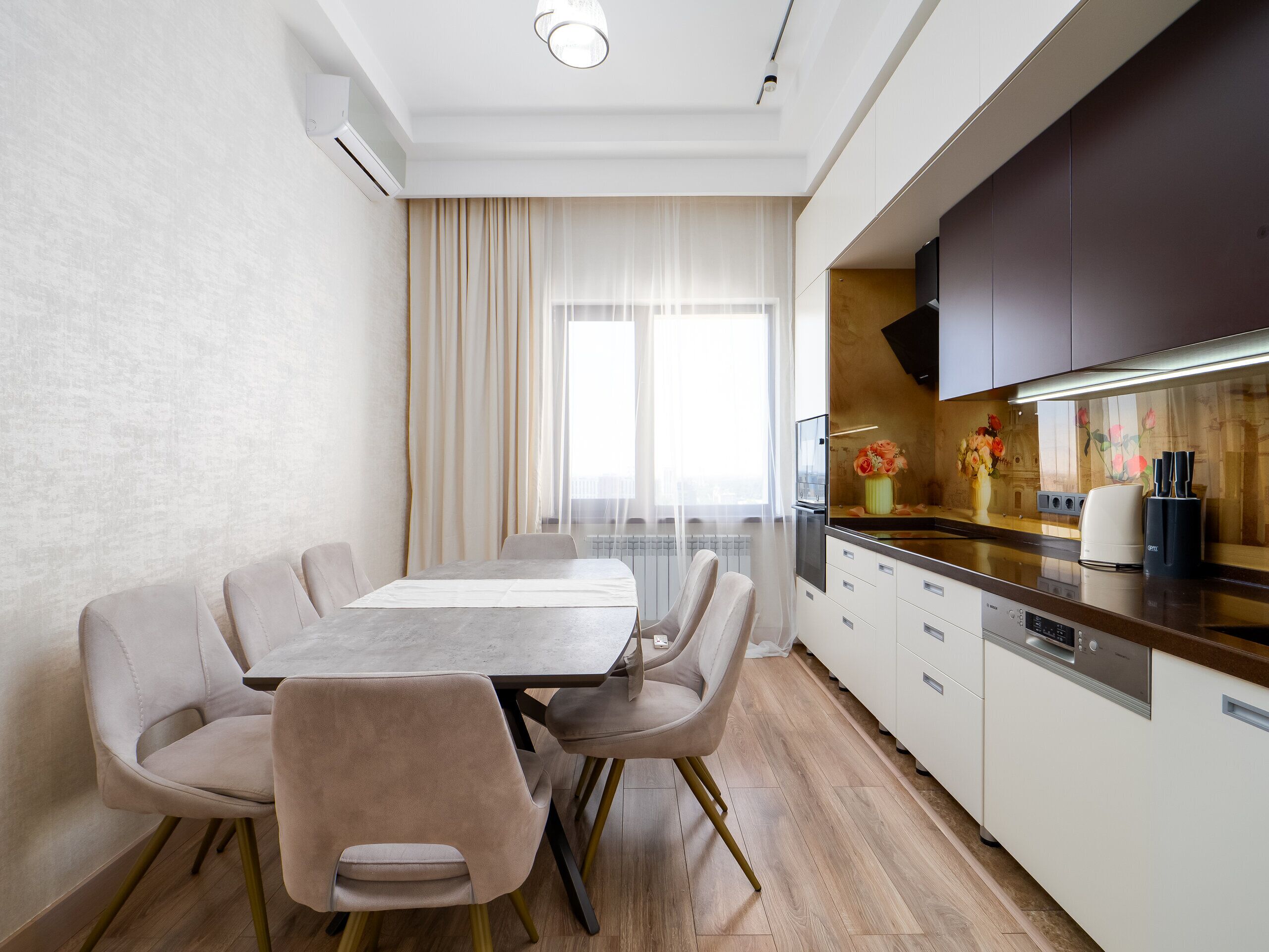 Una cocina moderna con comedor, que cuenta con una mesa larga, sillas y vistas a la ciudad a través de amplios ventanales.