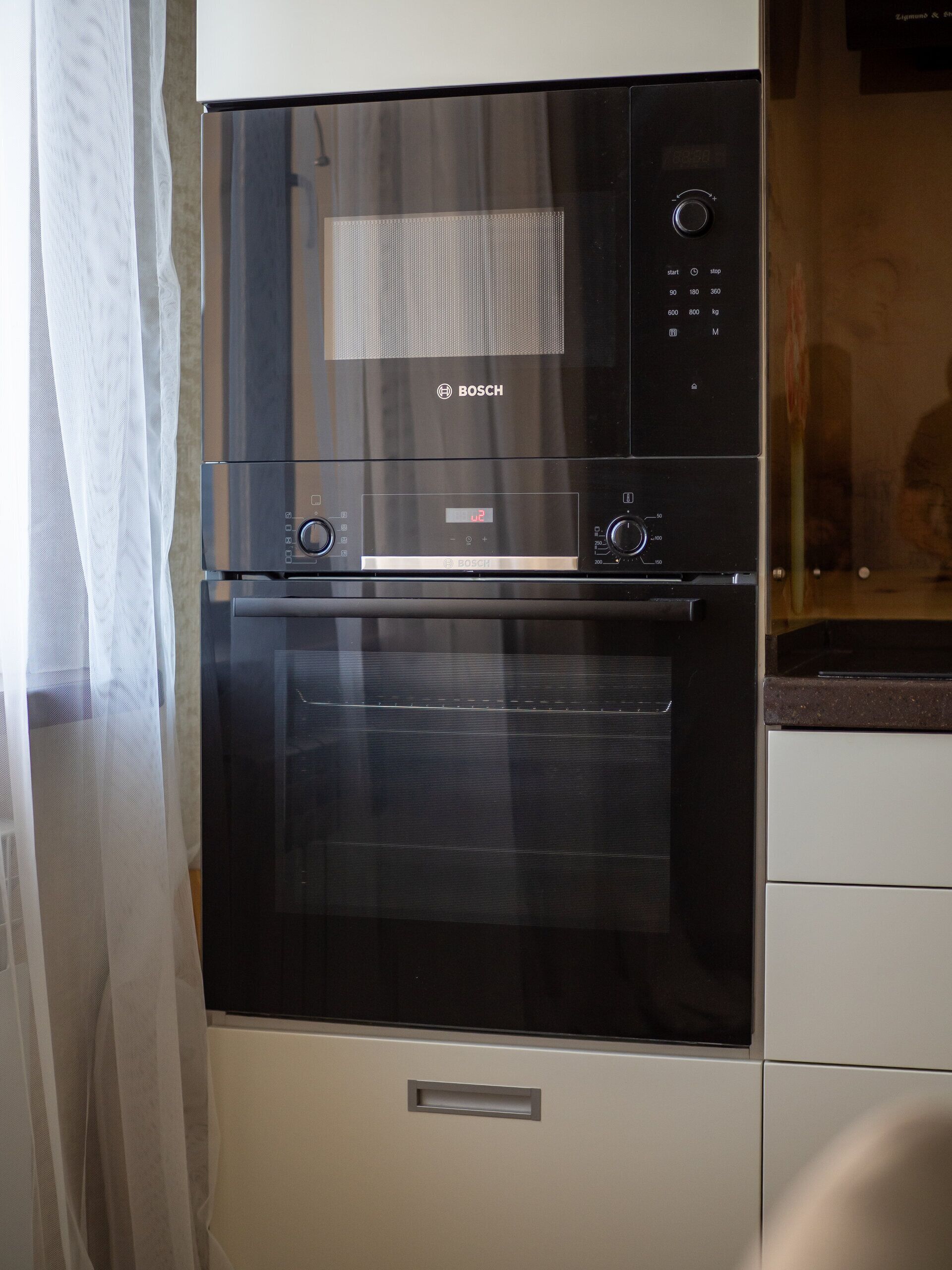 Una cocina con horno Bosch y microondas, una campana extractora de acero inoxidable y un armario blanco.