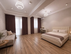 A modern bedroom with a large bed, a sofa, a desk, and a chair. - Spacious 4-room apartment (Almaty)