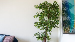 Ein Zimmer mit einem blauen Sofa, einem Blumentopf und einem Bild an der Wand.