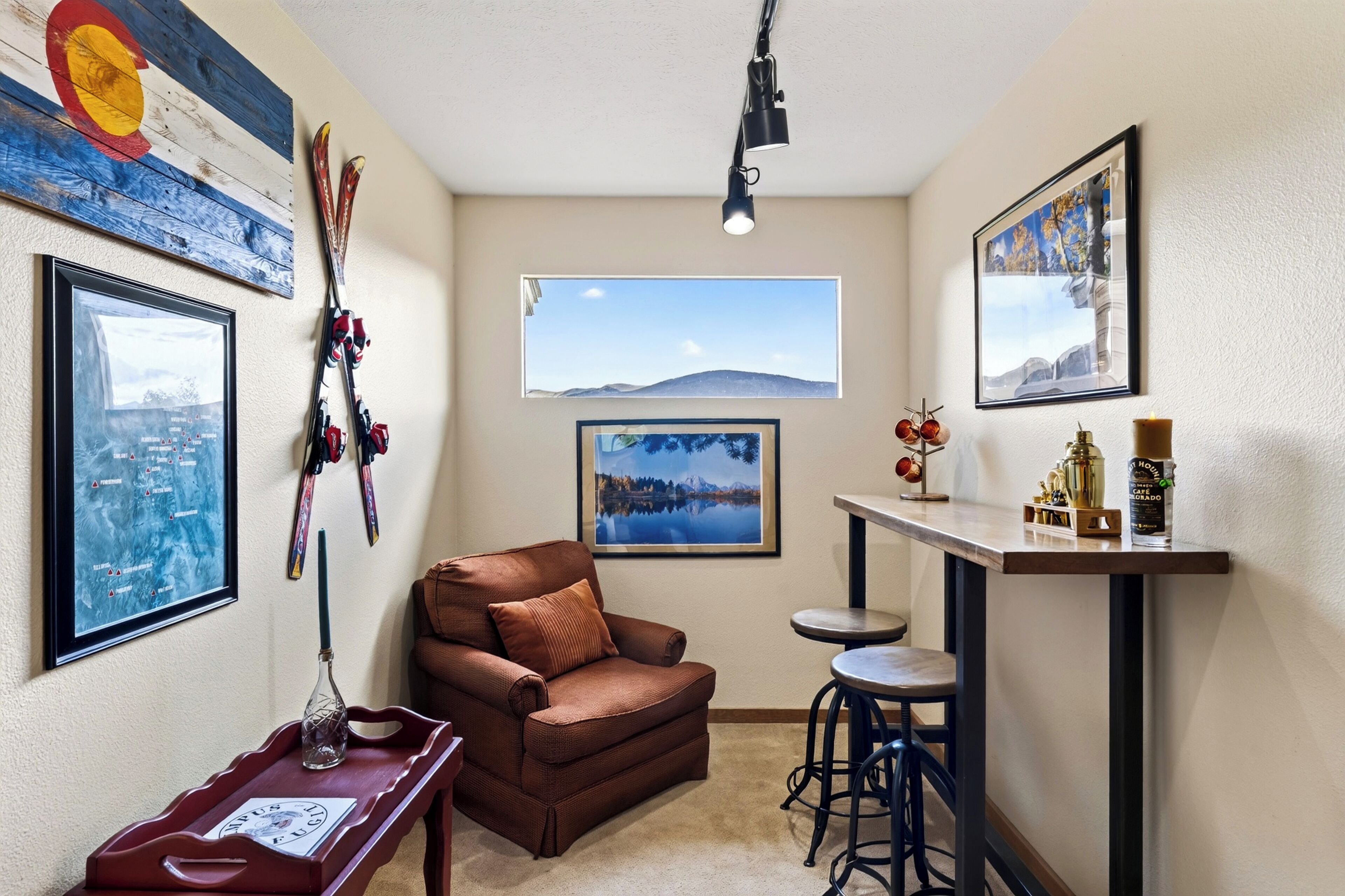 Een gezellige kamer met een bruine bank, een klein tafeltje met dienblad, een bar met barkrukken, en ski-uitrusting aan de muur.
