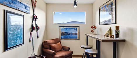 Ein gemütliches Zimmer mit einem braunen Sofa, einem kleinen Tisch mit Tablett, einer Bar mit Hockern und Skiausrüstung an der Wand.