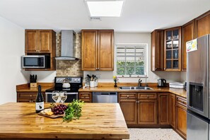 A modern kitchen with wooden cabinets, a built-in microwave, a gas stove, a dishwasher, and a stainless steel refrigerator. - Buttonwood Corner | Midtown Key West • Pool + Tropical Patio | Near Beaches (Key West)